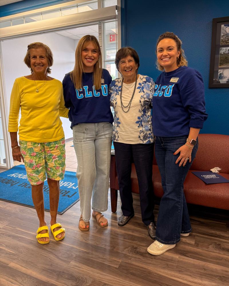 Frances Price smiling in a blue and white floral top, standing with her daughter and two CLCU team members inside the credit union