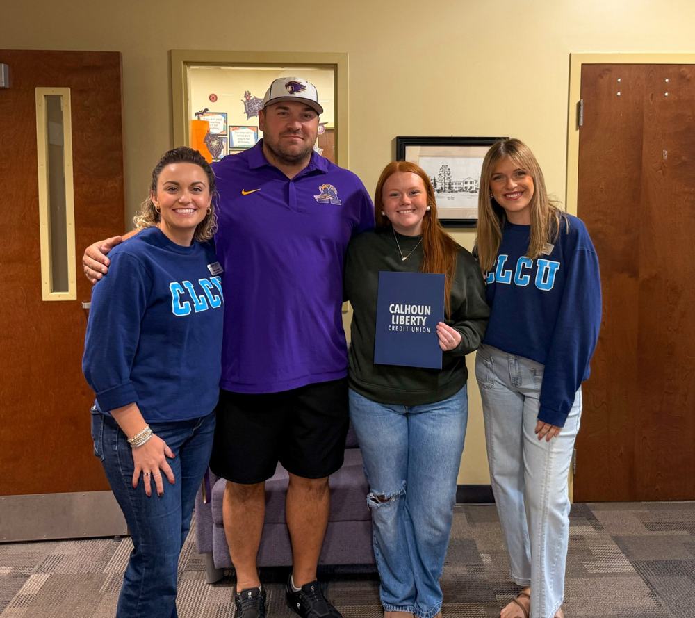 Taylor Hall holding her Calhoun Liberty Credit Union award folder, standing with her school principal and two CLCU team members
